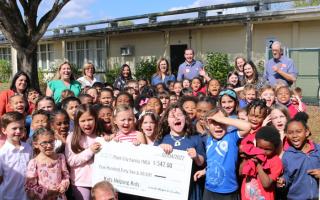 thirty elementary school children present check to the YMCA in February 2022 outside of the school