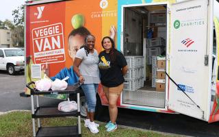Two women in front of the Veggie Van with food in bags.